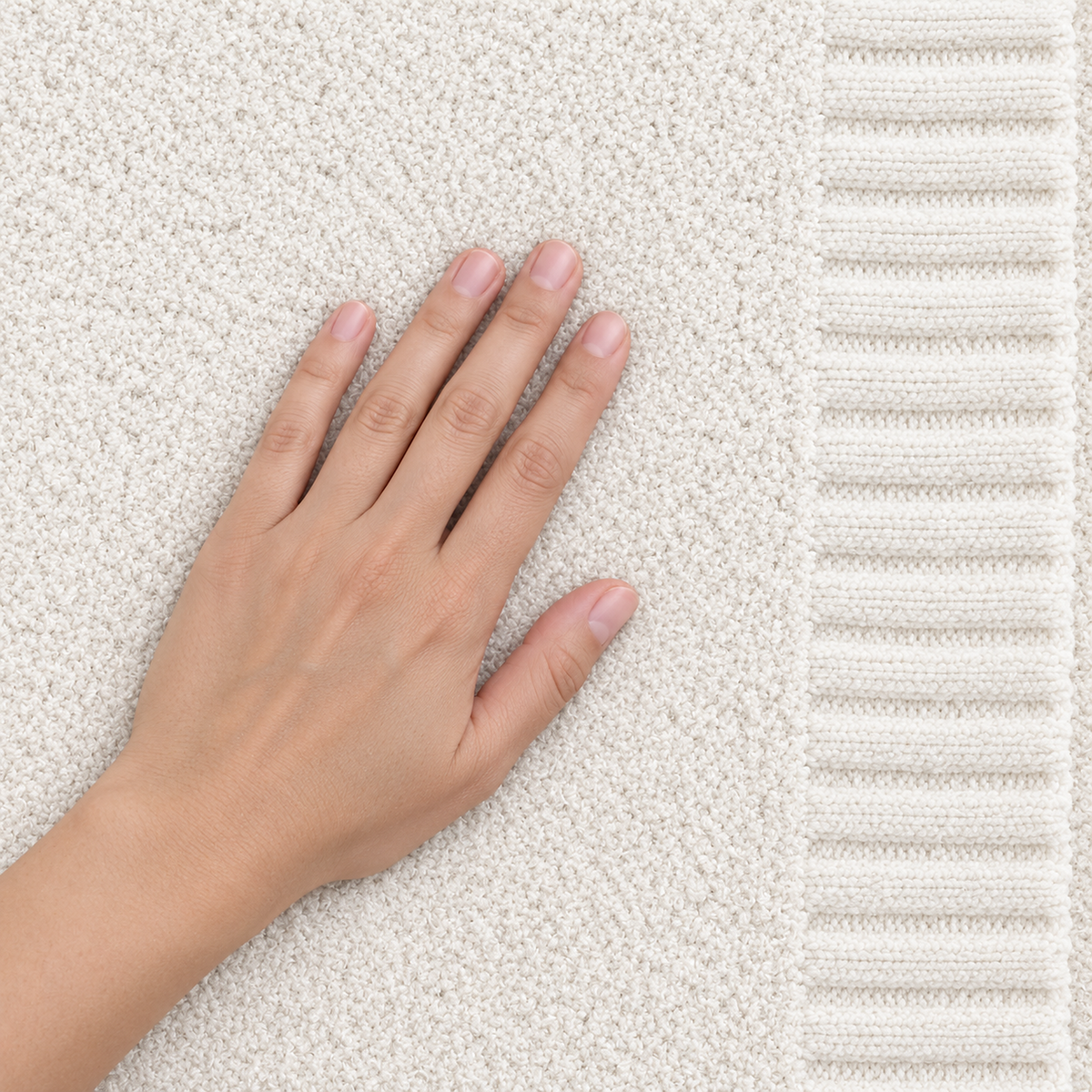 Calemira ivory throw blanket with an adult hand resting on its fine heathered knit surface