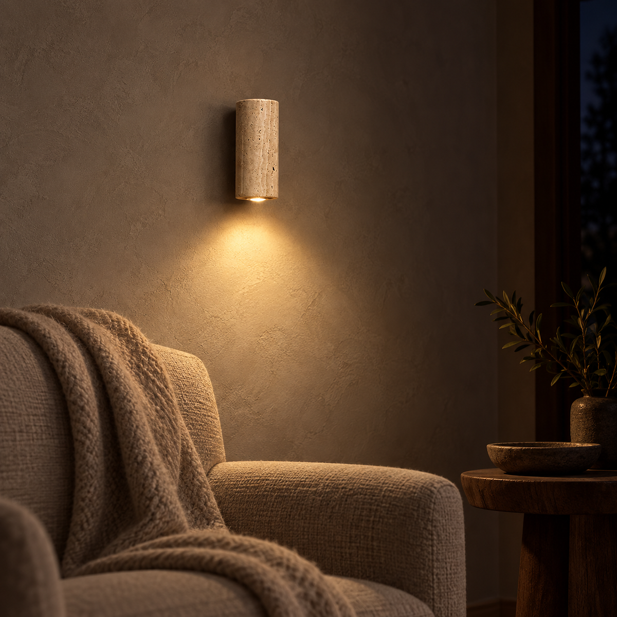 Cimorela wall light in travertine and walnut glowing beside an armchair at night