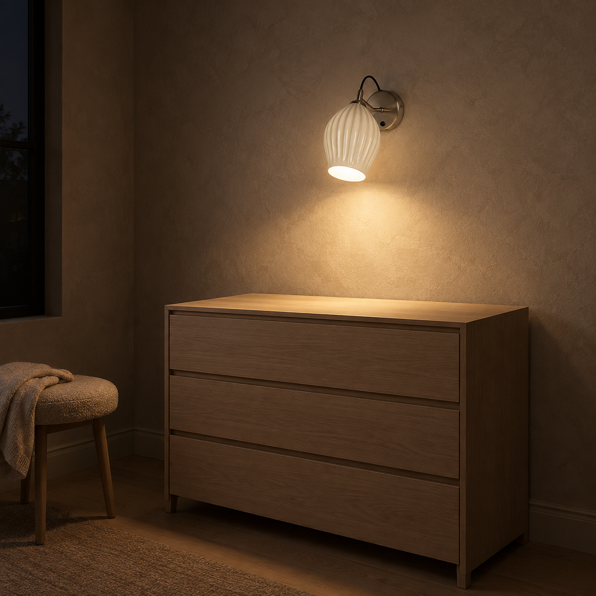 Comirel chrome bedside wall light lighting an empty chest of drawers at night