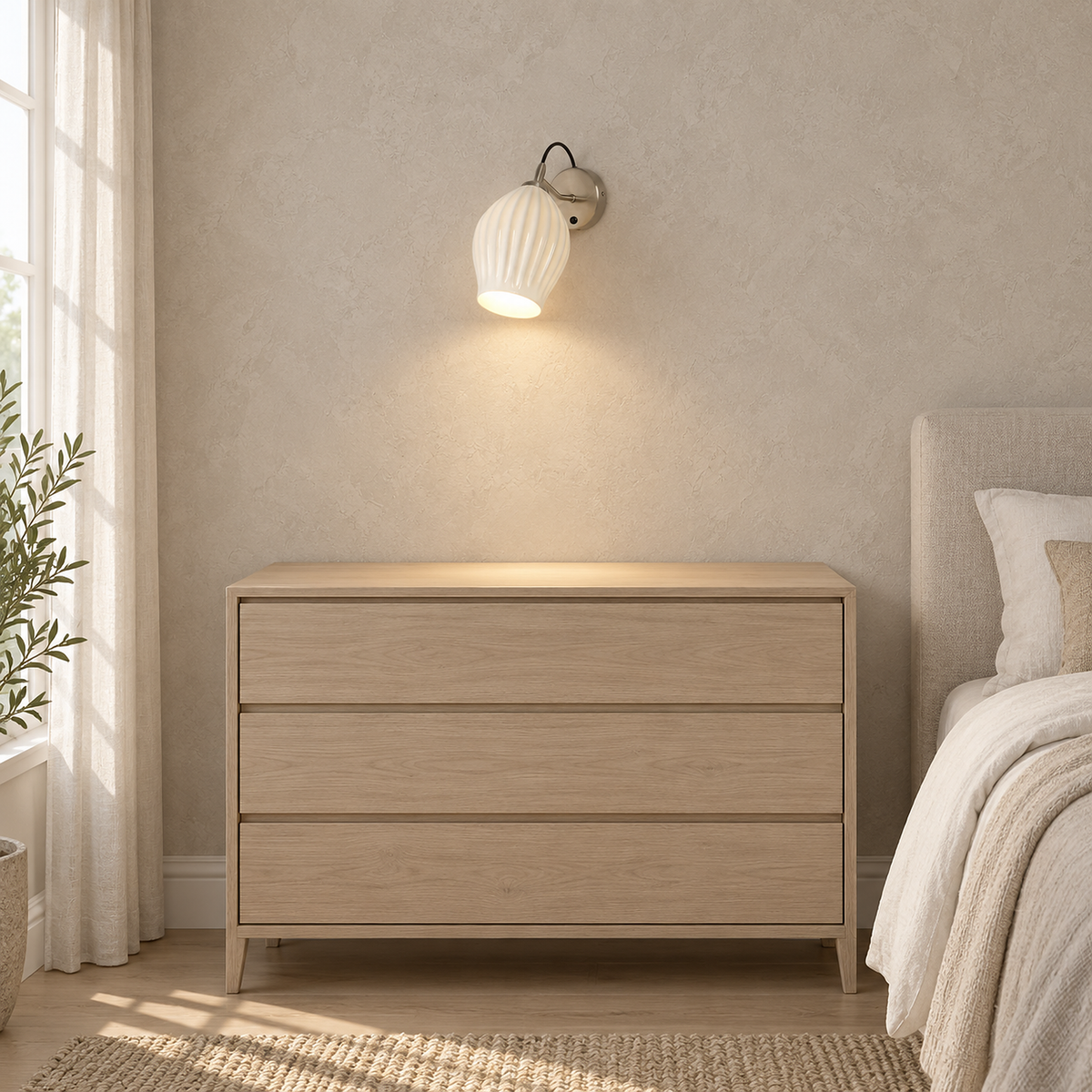 Comirel chrome bedside wall light lit above an empty bedroom dresser in daylight