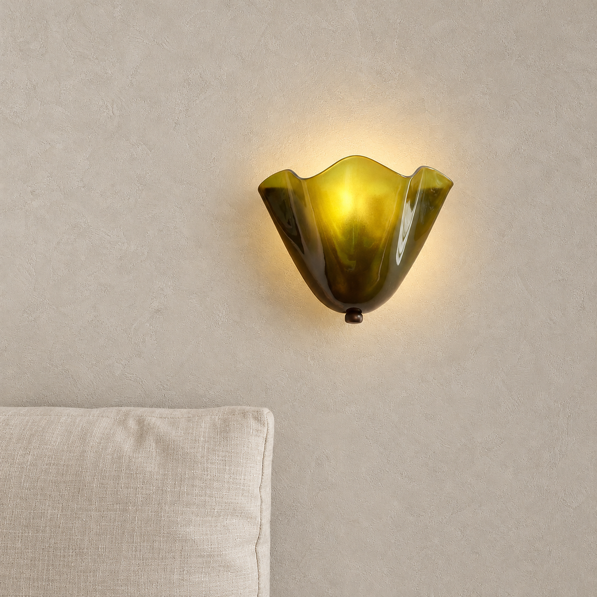 Ilsaren green plug in wall sconce lit softly, showing the sculptural folds of its glass shade