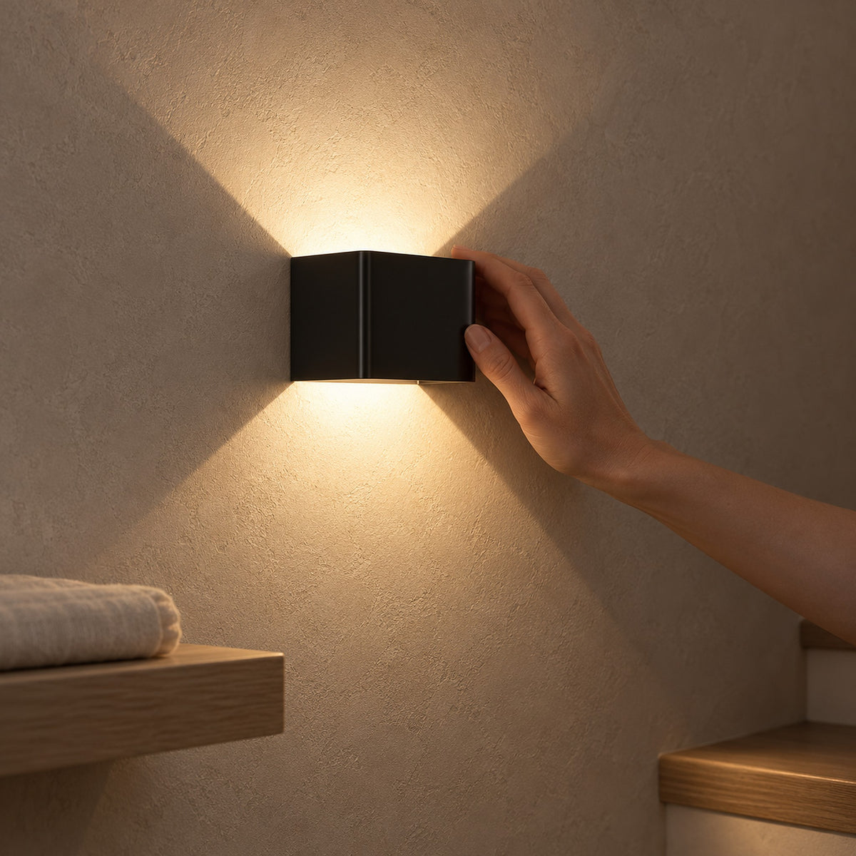Ivelmo Black battery operated wall sconce casts warm light up and down beside wooden stairs as a hand touches it