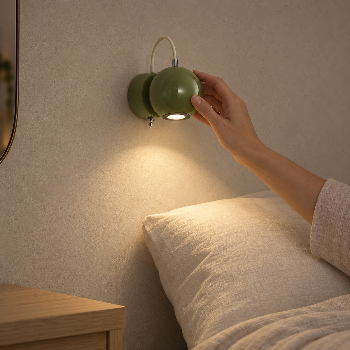 Lirema Green hardwired wall light above a bed, with a hand touching the lamp and a wooden bedside table.