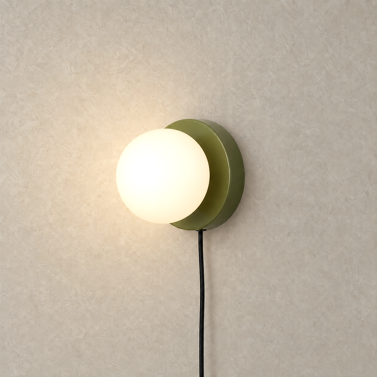 Memilora green bedside wall light lit against warm greige plaster on a plain plate
