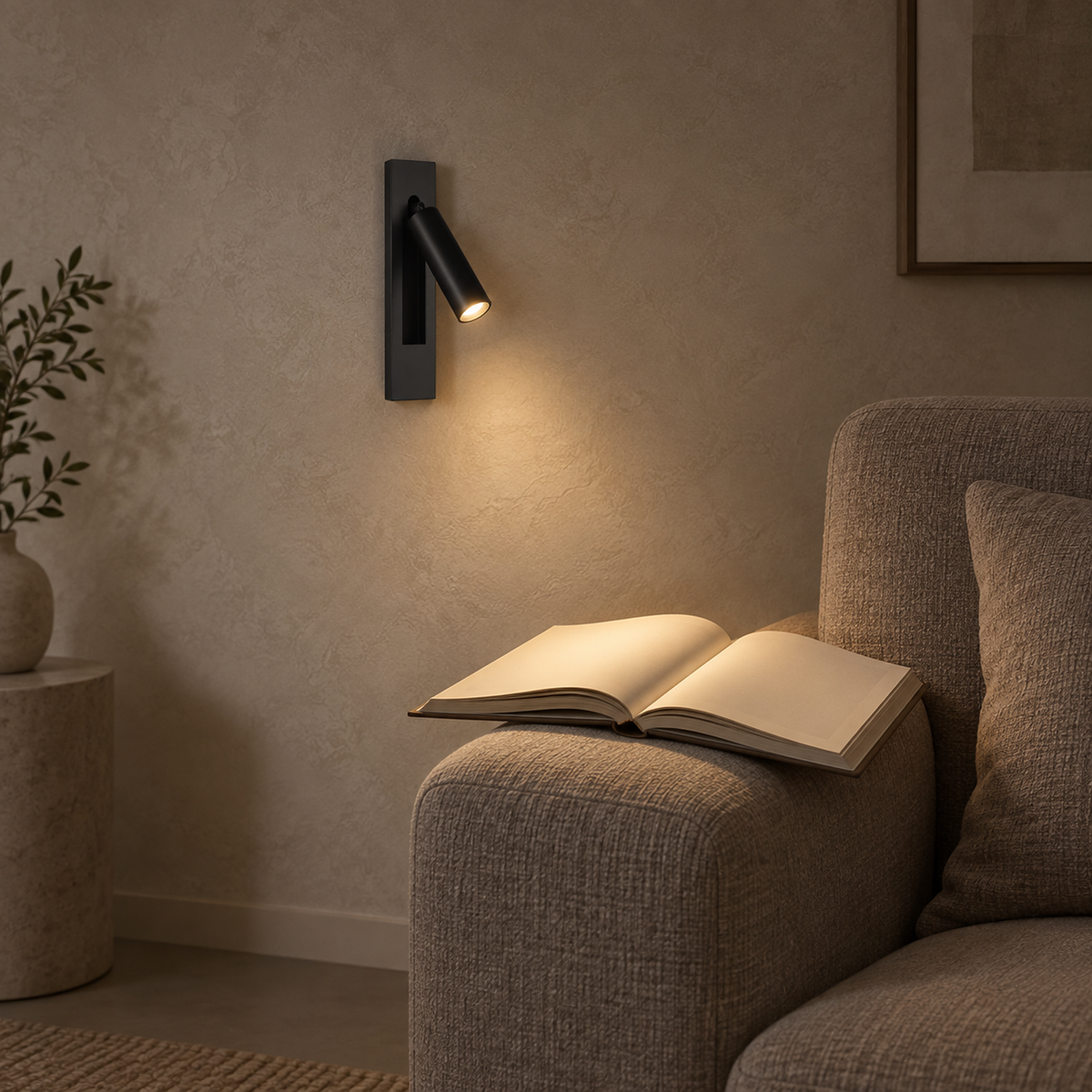 Menaliro black LED wall sconce aimed at a book resting on a chair arm in a living room