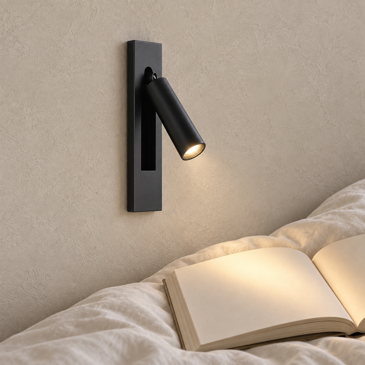 Menaliro black LED wall sconce lit above a book on a guest bedside table in daylight