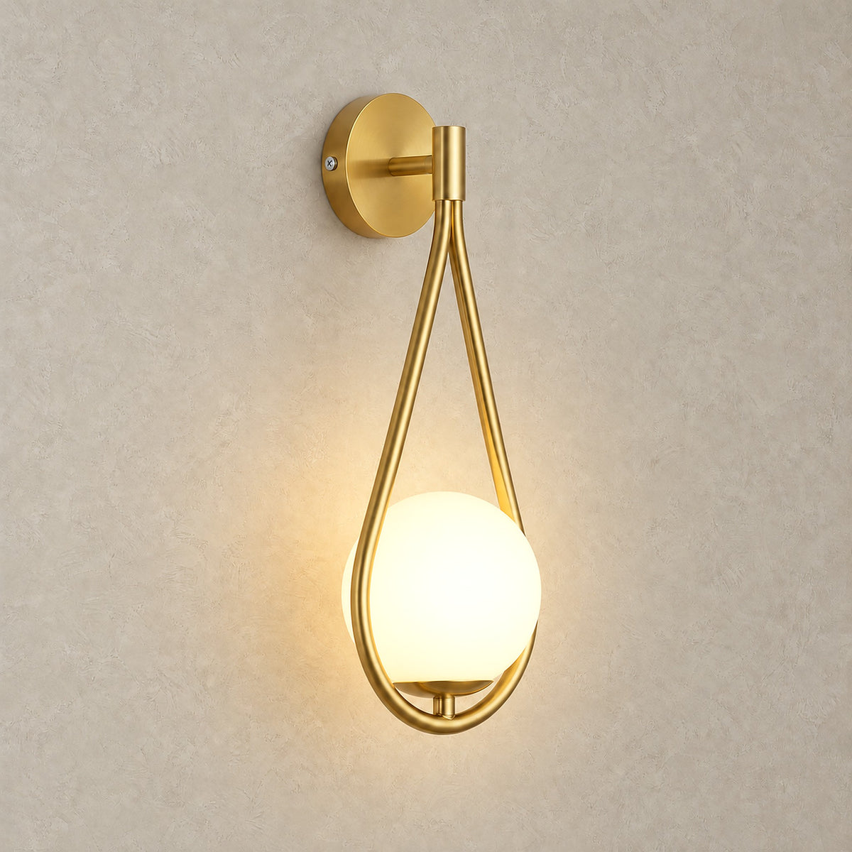 Mesaril gold bedside wall light, lit, its glass shade glowing against a plain backdrop