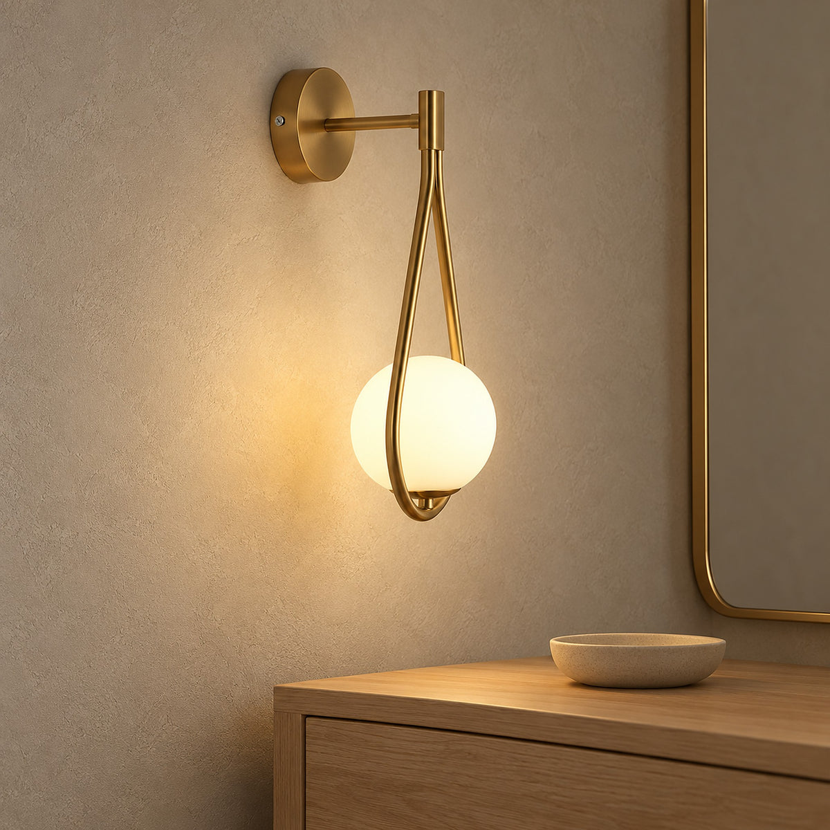 Mesaril gold wall sconce lit in a dressing room beside a metal mirror