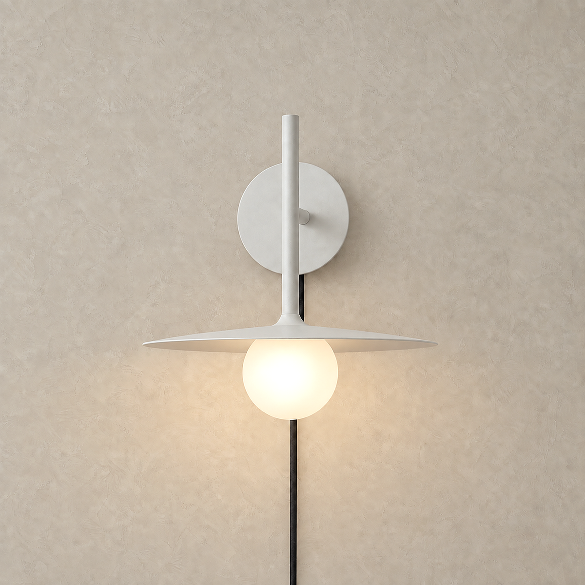 Milvaro white wall sconce lit in a straight front view of the metal disc and frosted globe