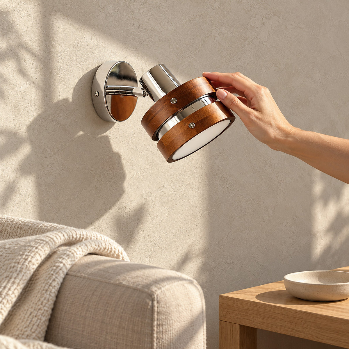 Nerilvo chrome and walnut wall lamp unlit, wood bands beside the edge of a living room sofa