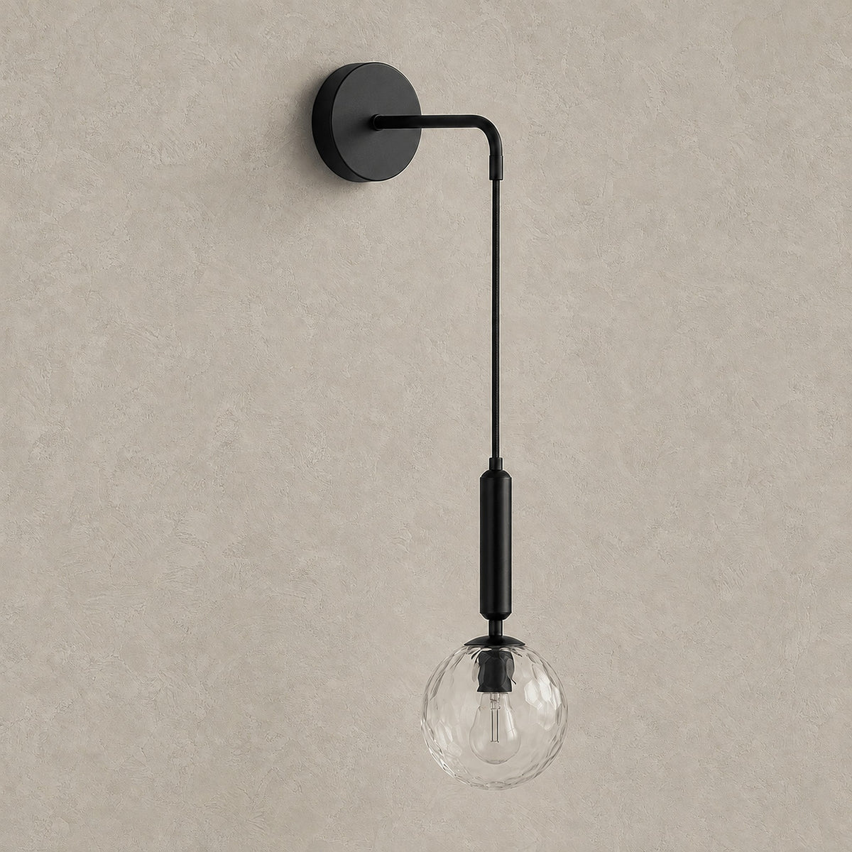 Orlamen black hardwired wall sconce with clear glass globe, unlit against greige plaster