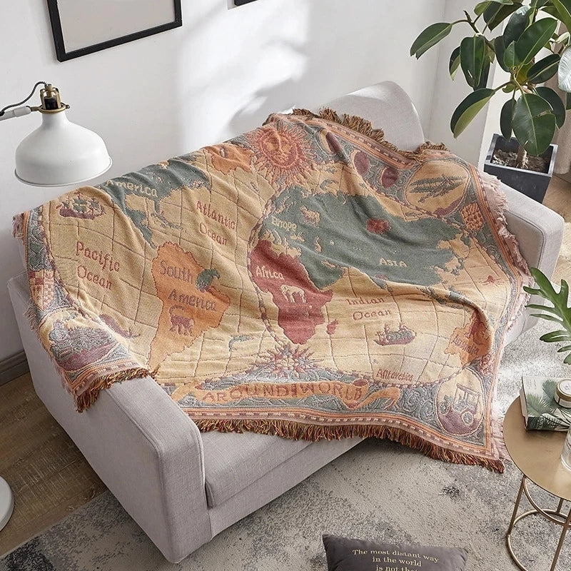 Saloveri world map throw blanket draped over a light gray armchair, showing its colorful map design and fringed edges.