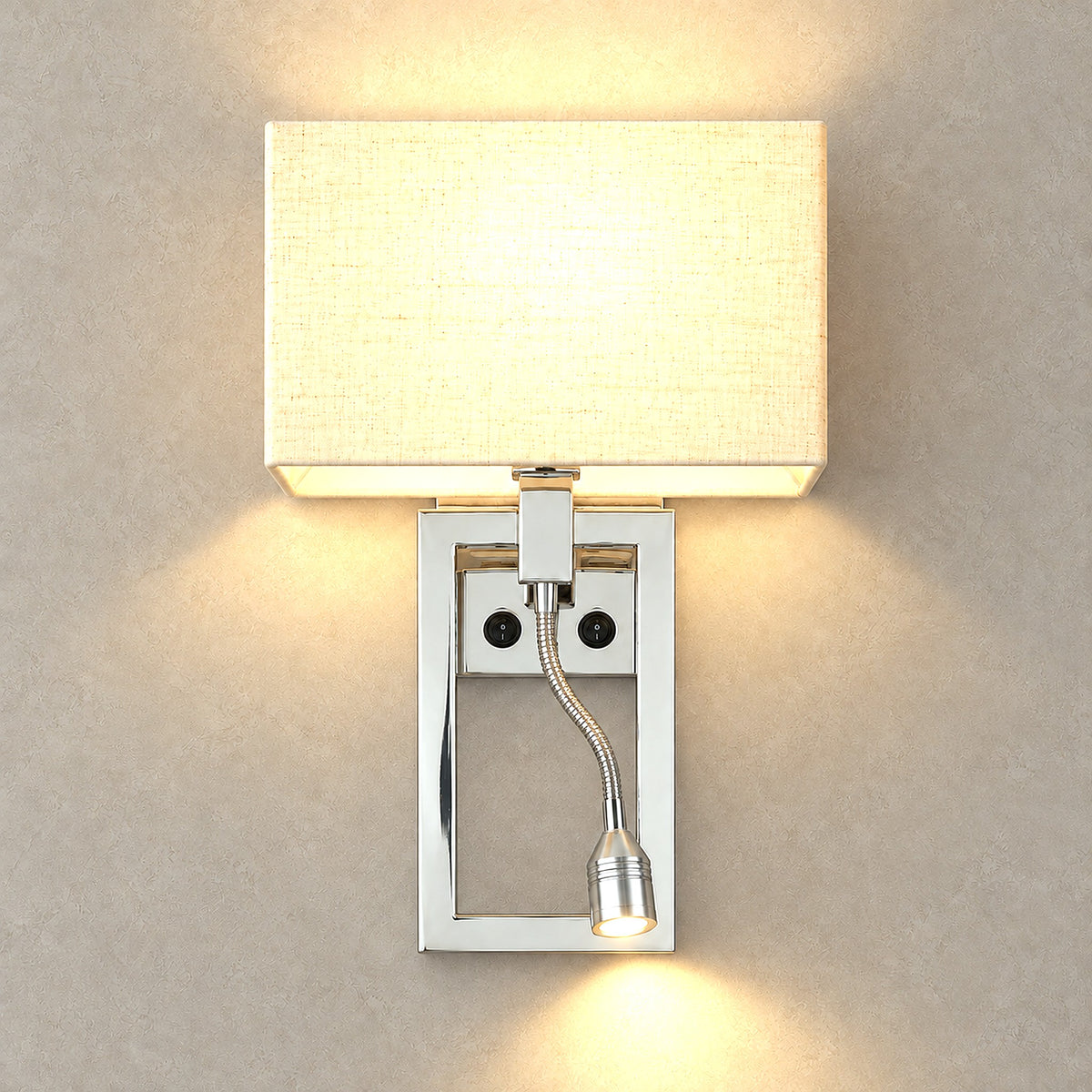 Silarno chrome hardwired wall light switched on, glowing through the fabric shade onto the wall above and below