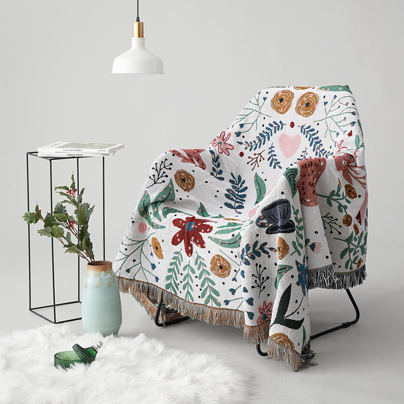 Tilmena tapestry throw blanket draped over an armchair, showing colorful botanical patterns and fringed edges.