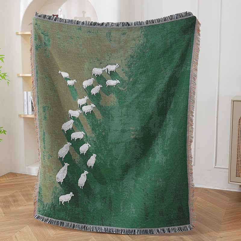Timarno green woven sheep throw blanket held upright indoors, showing its full sheep pattern and fringed edges.