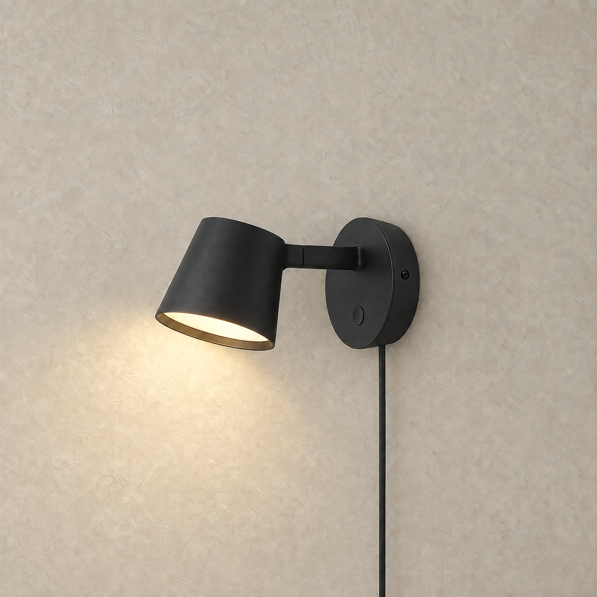 Tisello black LED wall sconce glowing against a warm greige plaster wall backdrop