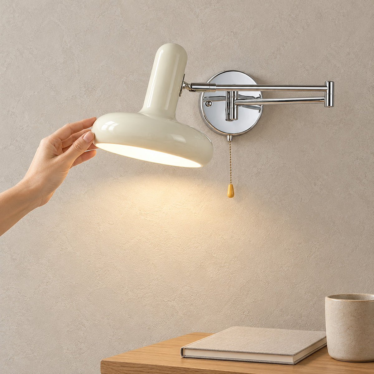Tivenola Cream hardwired wall sconce with silver backplate and pull chain, a hand touching the lit shade