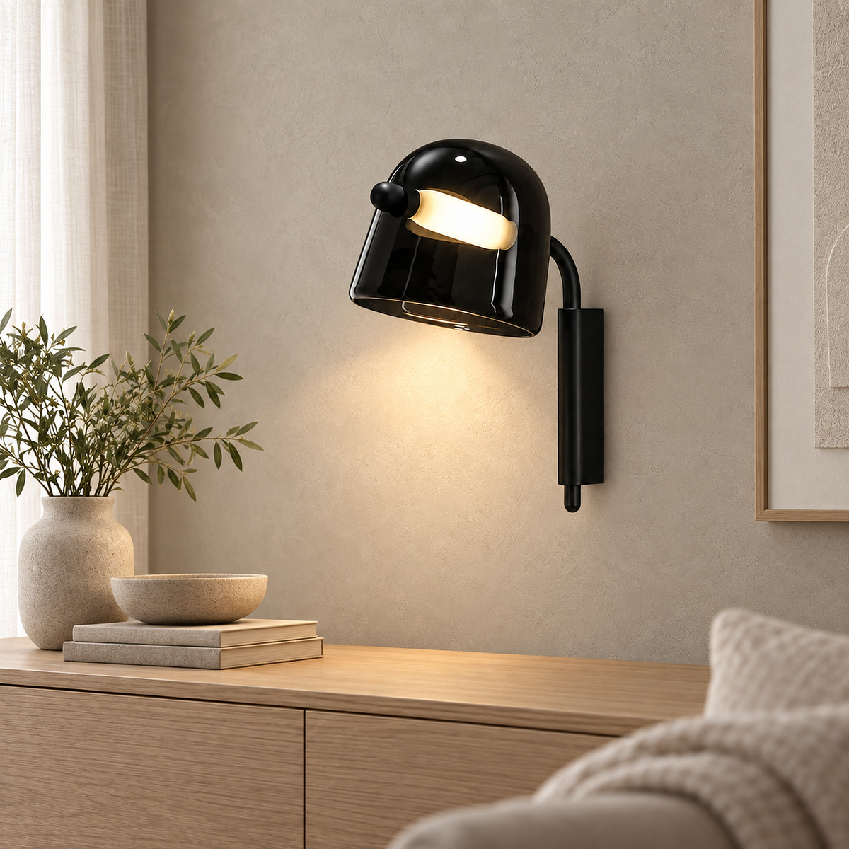 Black Tavessi wall sconce lit as a dark shape against pale plaster above an oak sideboard