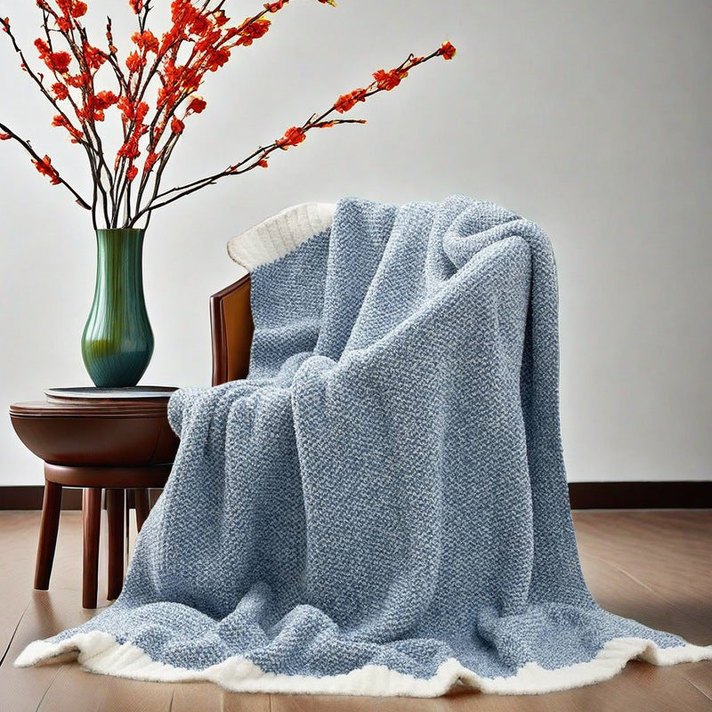Calemira Pale Blue throw blanket for couch with white trim draped over an armchair beside a dark wood table.