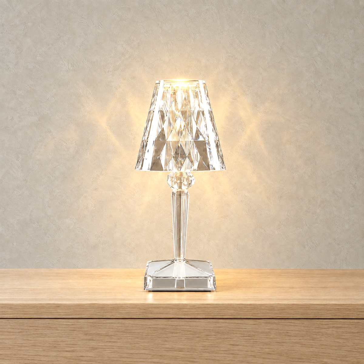 Cerilan clear table lamp lit against warm greige plaster, faceted shade glowing