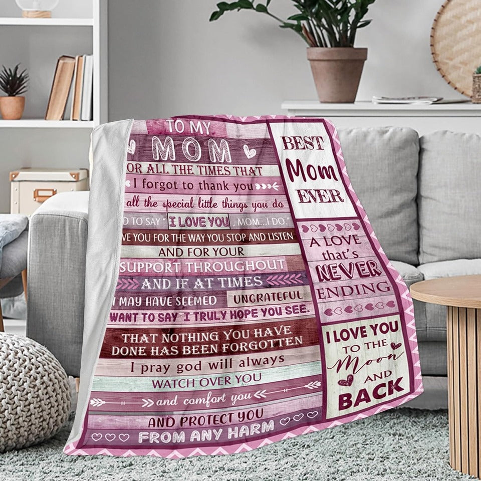 Elmisa mom fleece throw blanket draped over a gray sofa, showing its pink message panel and white fleece backing.