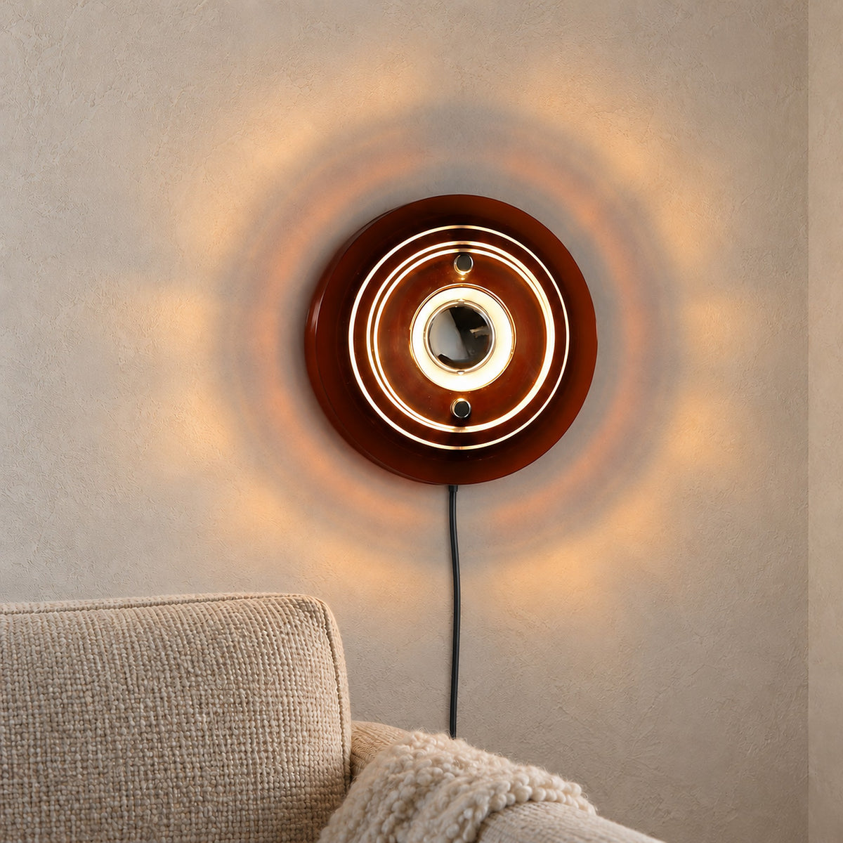 Elsarvo brown plug in wall lamp glowing above an oatmeal armchair in a daylit alcove