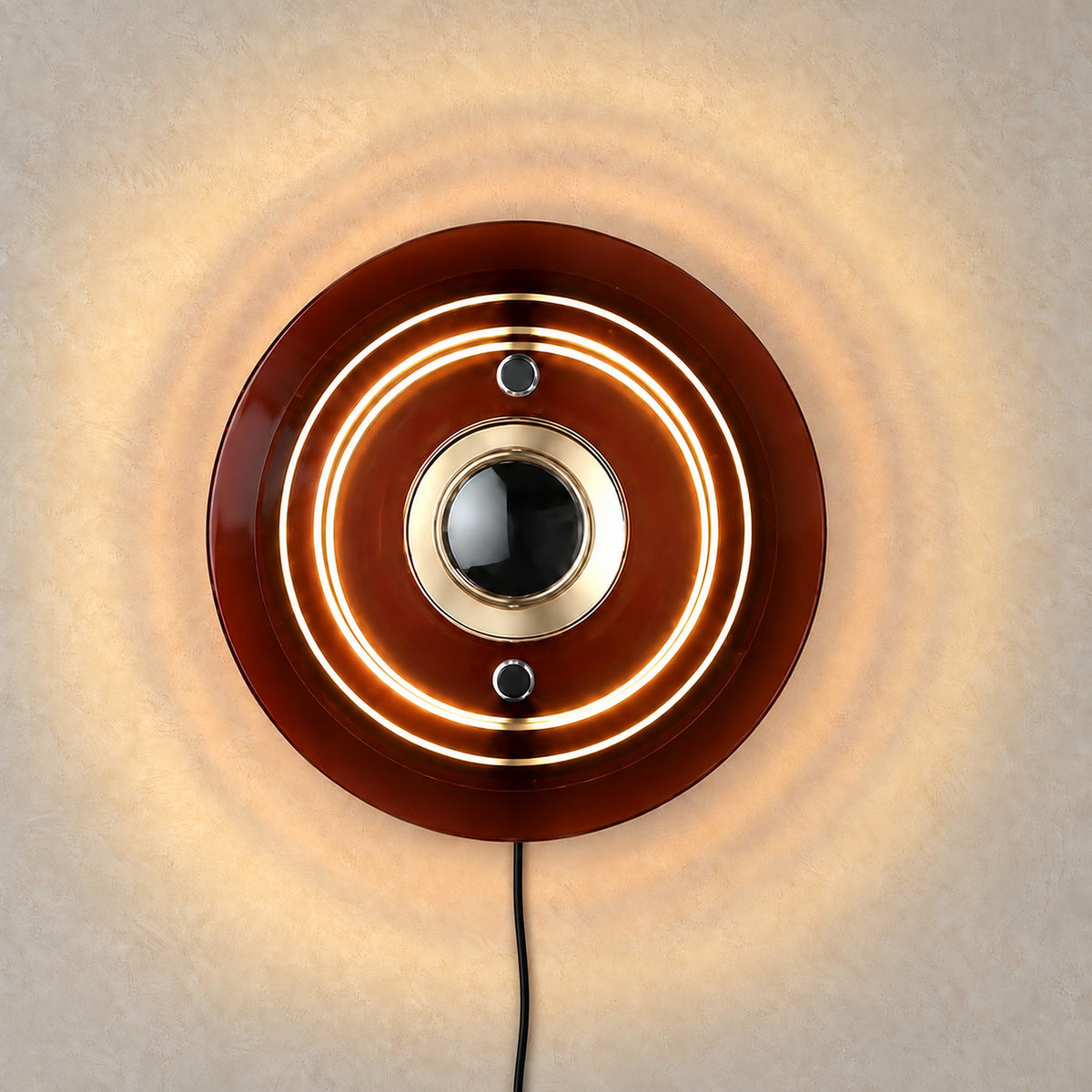 Elsarvo brown wall sconce lit against warm greige plaster, light spilling between the acrylic rings
