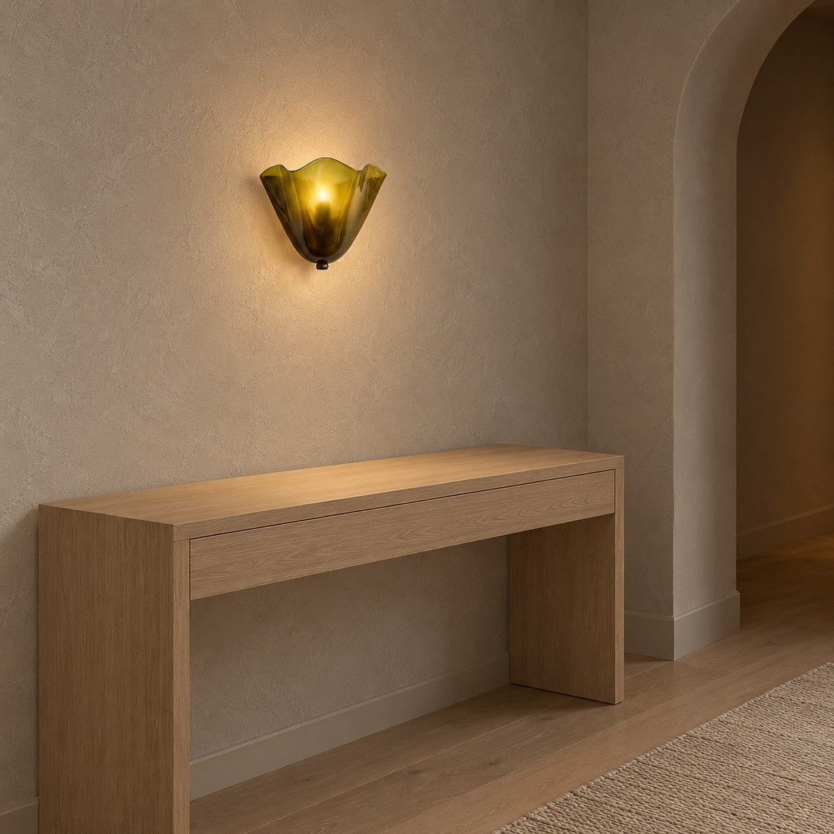 Ilsaren green wall lamp lit above a clear hallway console, its folded glass glowing