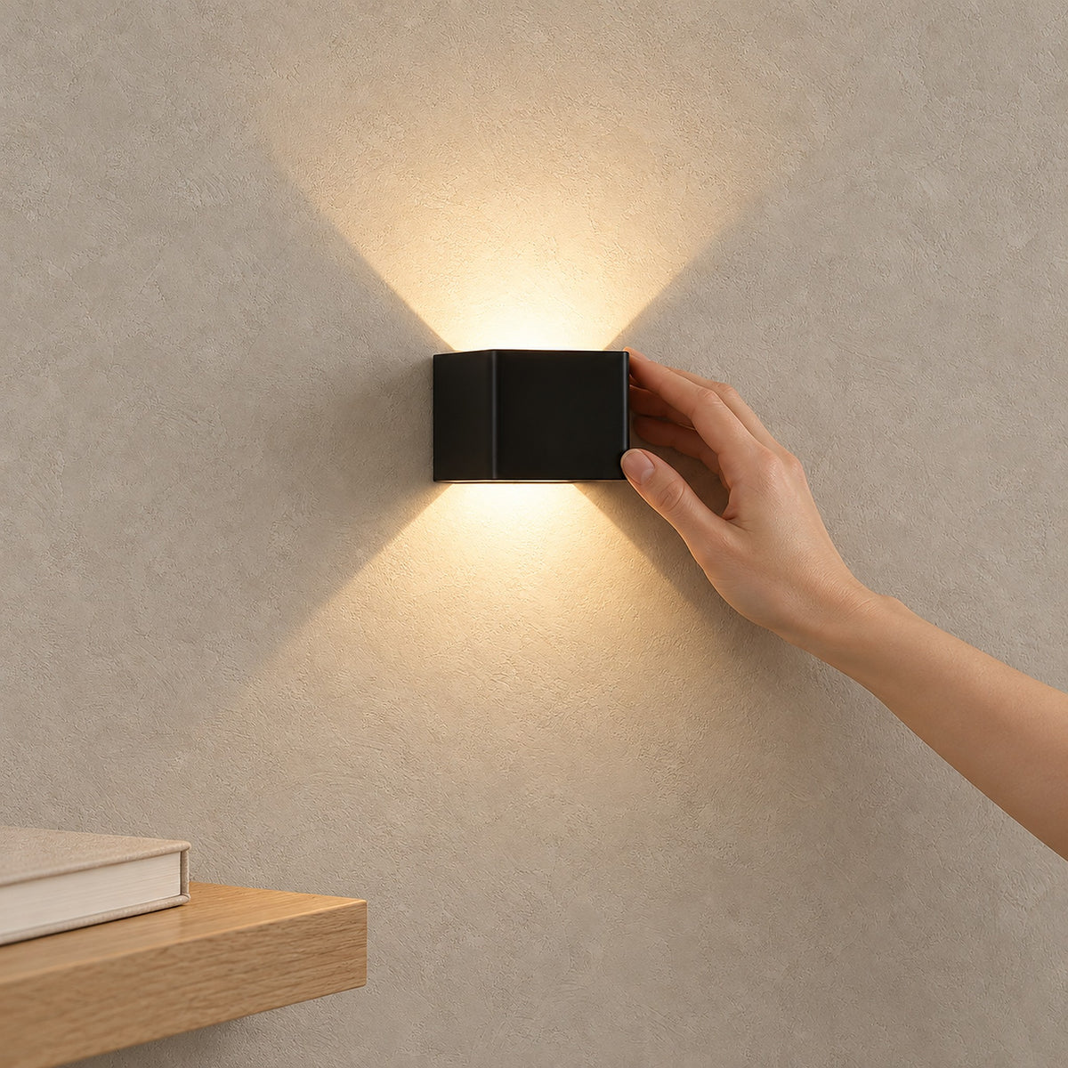 Ivelmo Black wall light casting warm light up and down a textured wall, with a hand touching it.