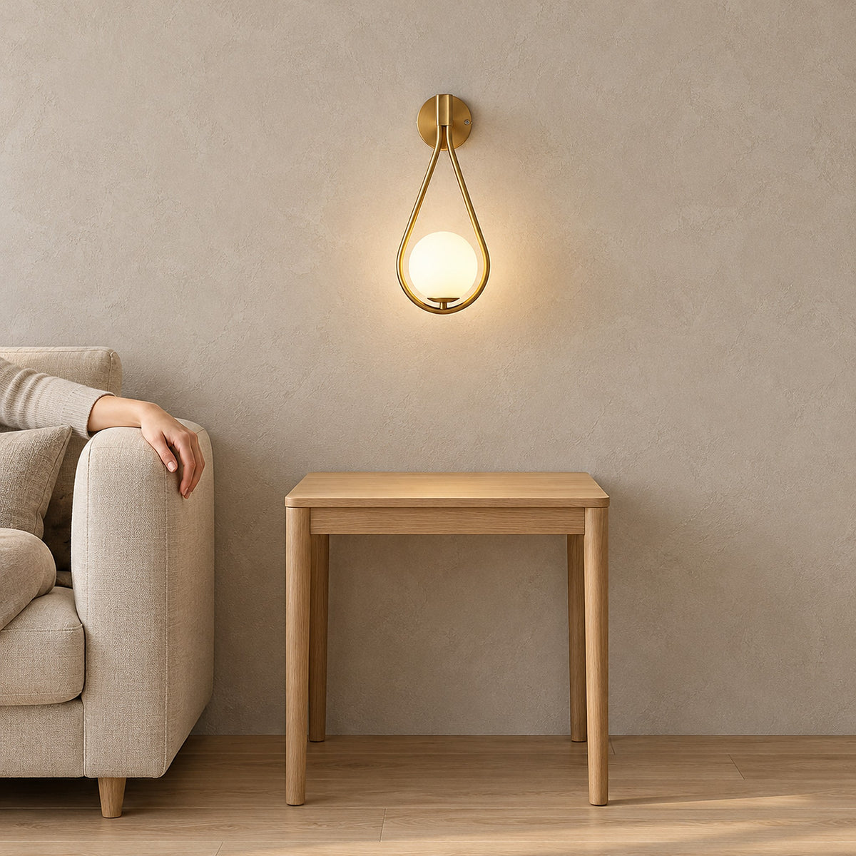 Mesaril Gold wall lamp with a glowing globe in a teardrop frame above a wooden end table beside a beige sofa