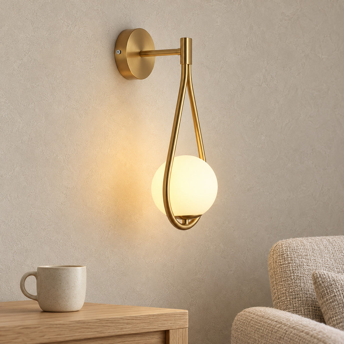 Mesaril gold wall lamp glowing in a reading corner beside an armchair and a cup
