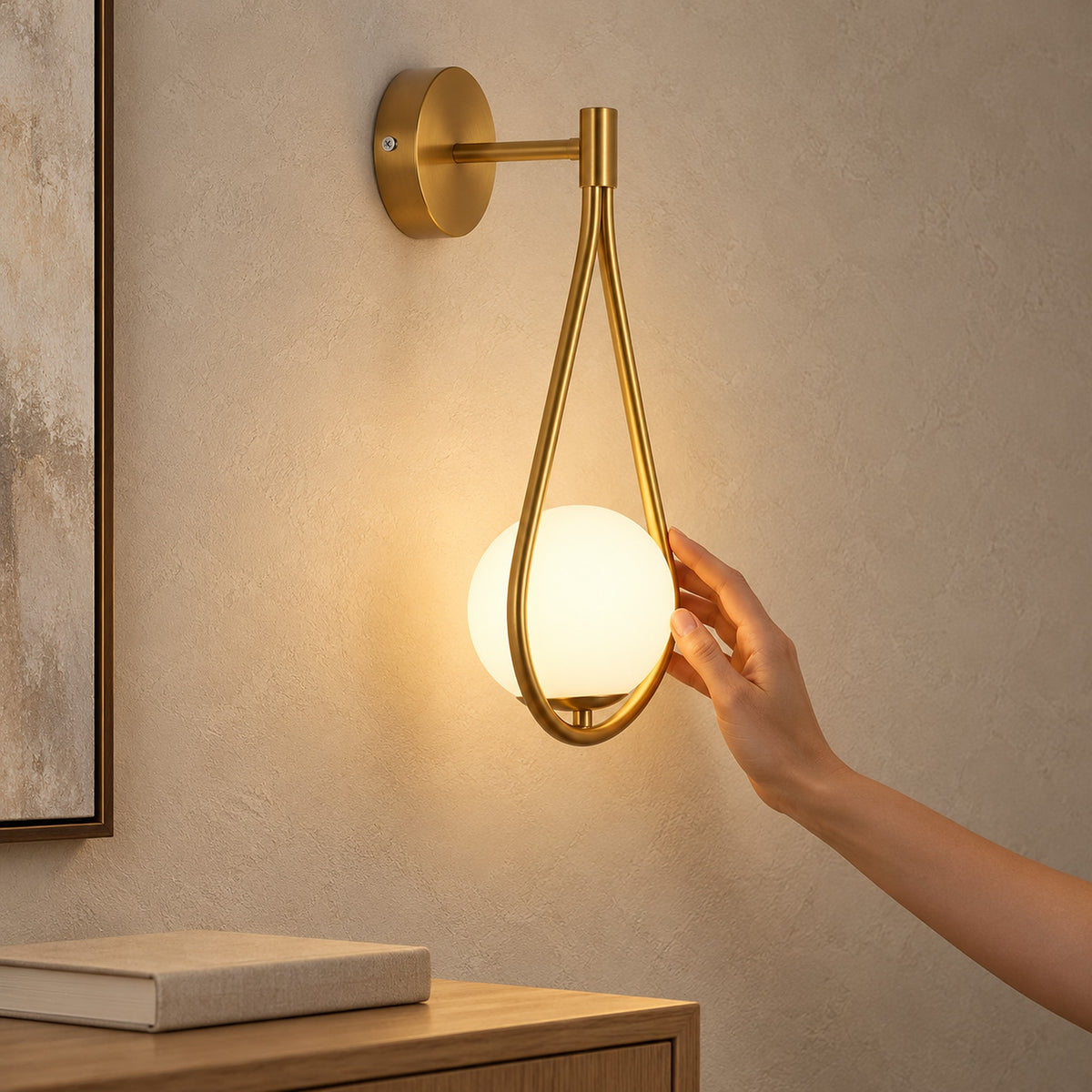 Mesaril Gold wall light with a glowing globe in a teardrop frame above a wooden cabinet with a book.