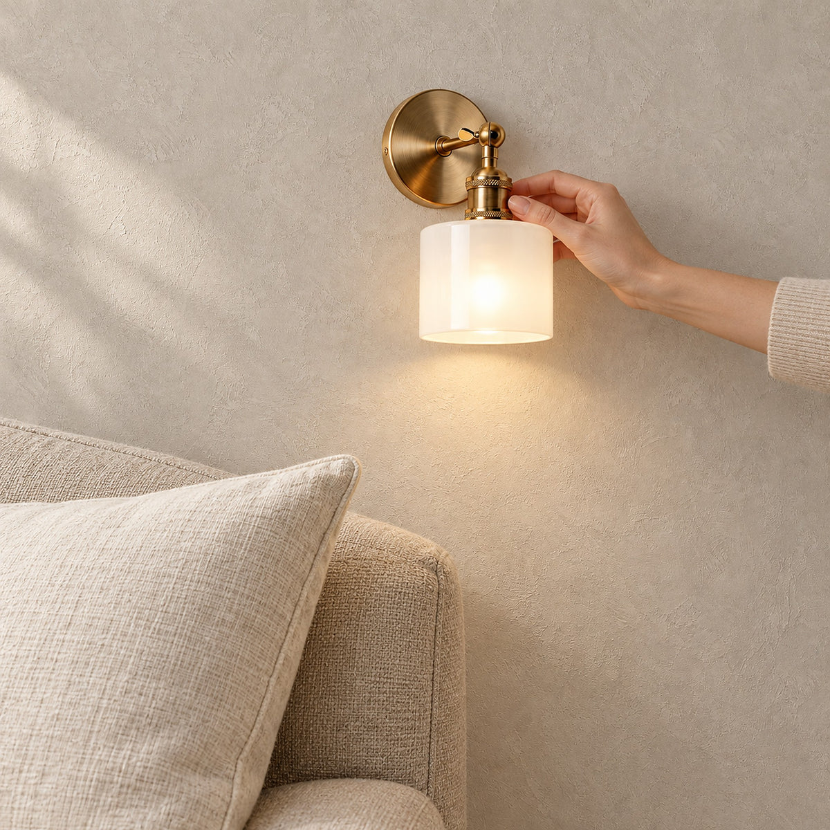 Nevalto White battery operated wall sconce lit beside a beige sofa, with a hand touching its brass hardware.