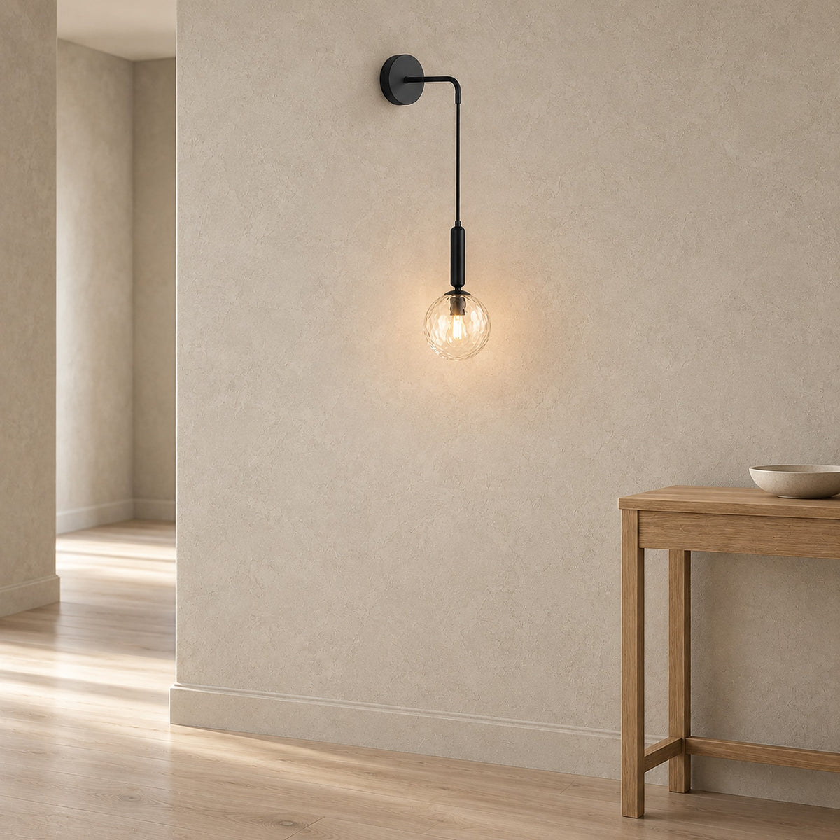 Orlamen black hardwired wall sconce glowing in a hallway, the wall below it left bare