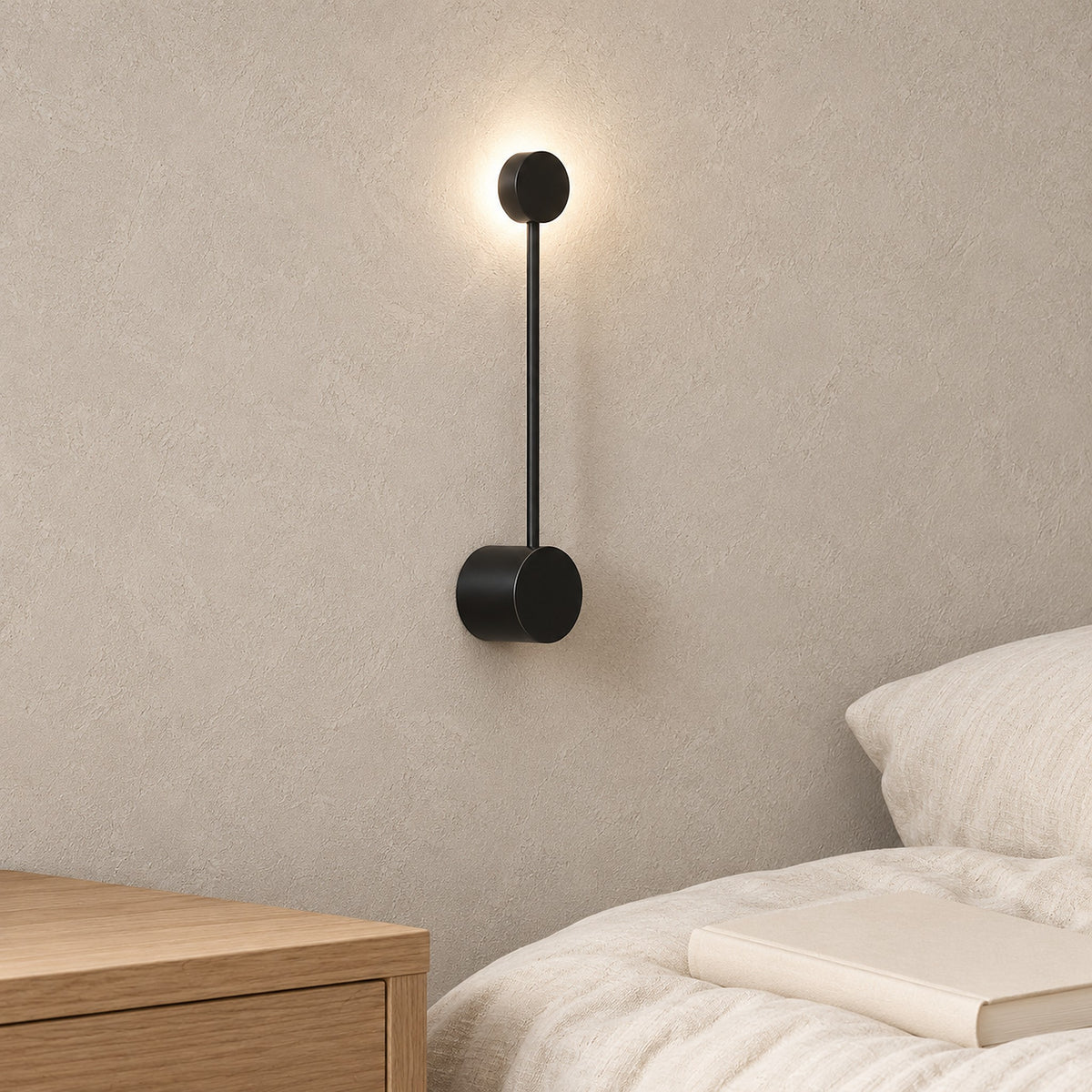 Rilameo black bedside wall light glowing above a clear bedside surface in a studio sleeping nook