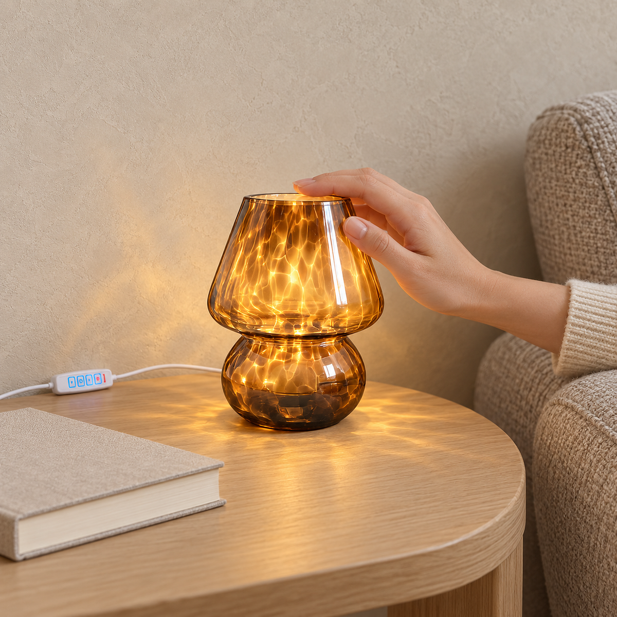 Rimelota Brown bedside lamp glowing on a wooden table beside an upholstered armchair, touched by a hand.