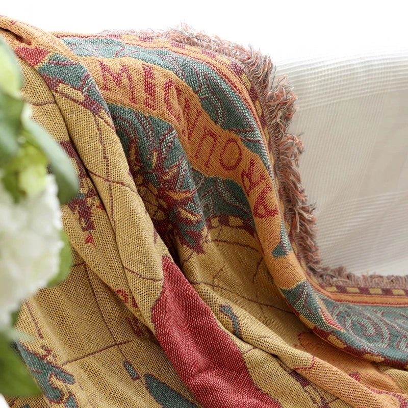 Saloveri world map throw blanket draped over a white sofa, showing the map pattern and fringed edges