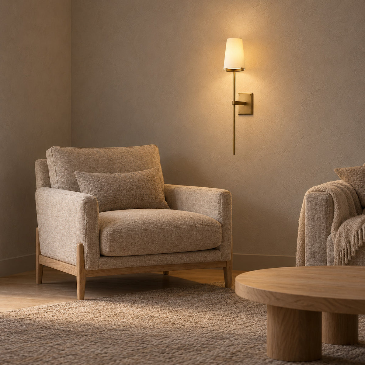 Savorel brass toned wall lamp with a glowing cream shade beside a beige armchair