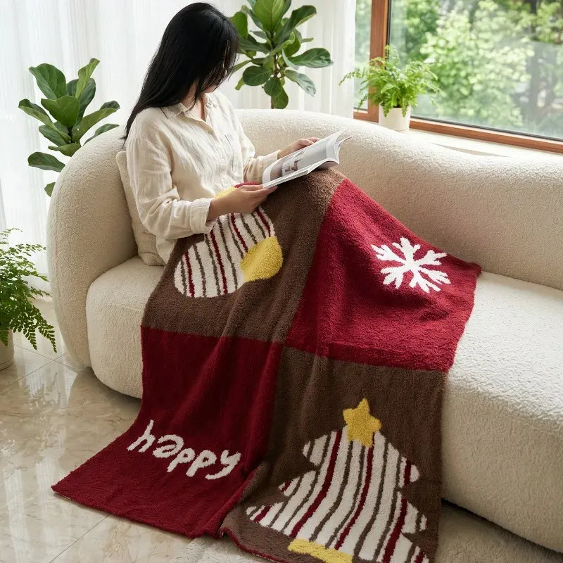 Senalio christmas fleece throw blanket over a reader's lap on a cream sofa, showing tree and snowflake motifs.
