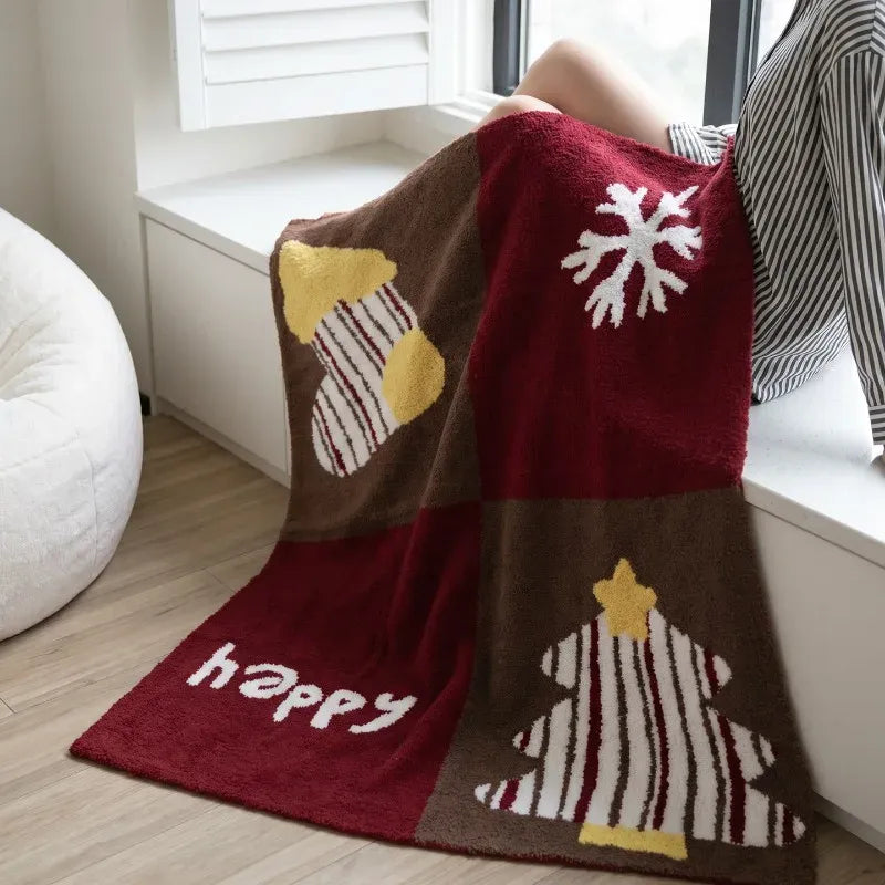 Senalio christmas fleece throw blanket draped over a lap by a window, showing stocking, snowflake and tree motifs.