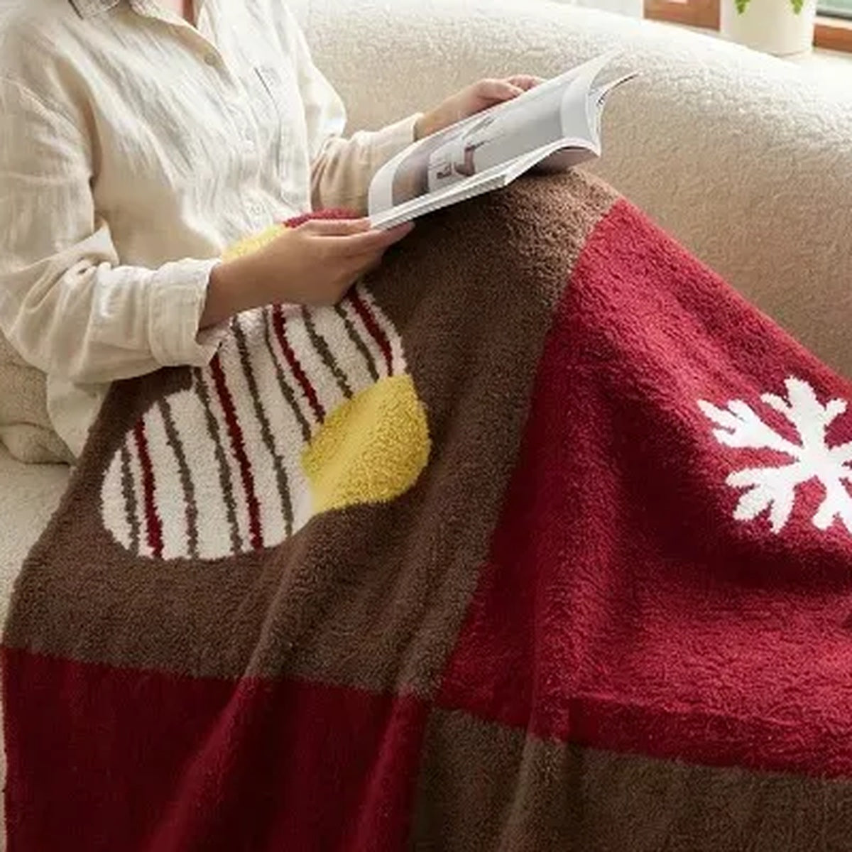 Senalio christmas fleece throw blanket draped over a seated reader's lap, showing red and brown panels and a snowflake.