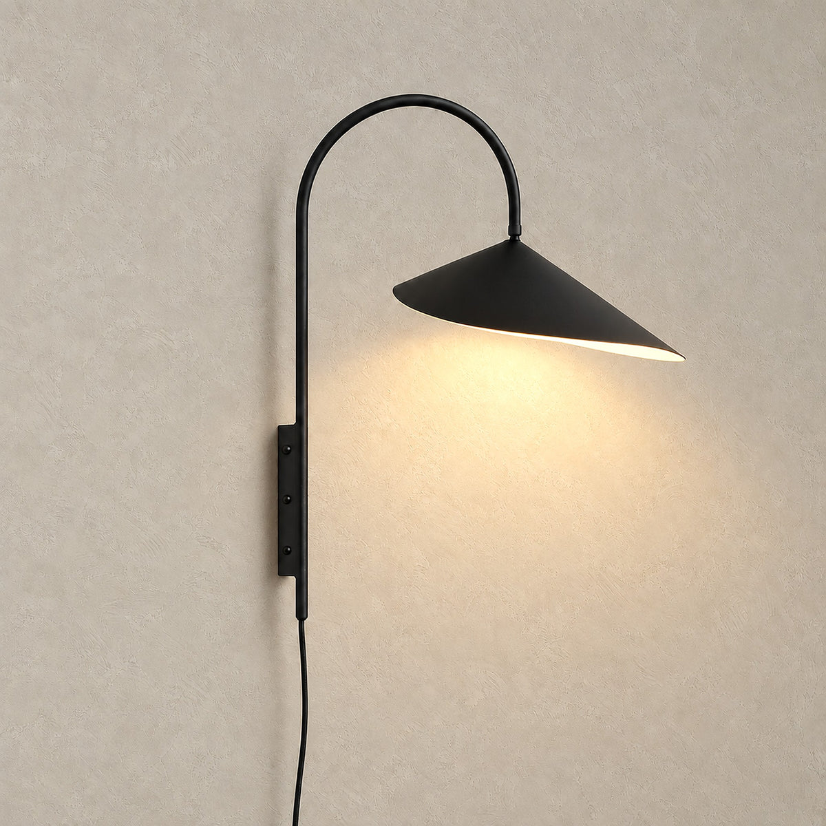 Talirsa black wall lamp switched on against warm greige plaster, showing its curved shade