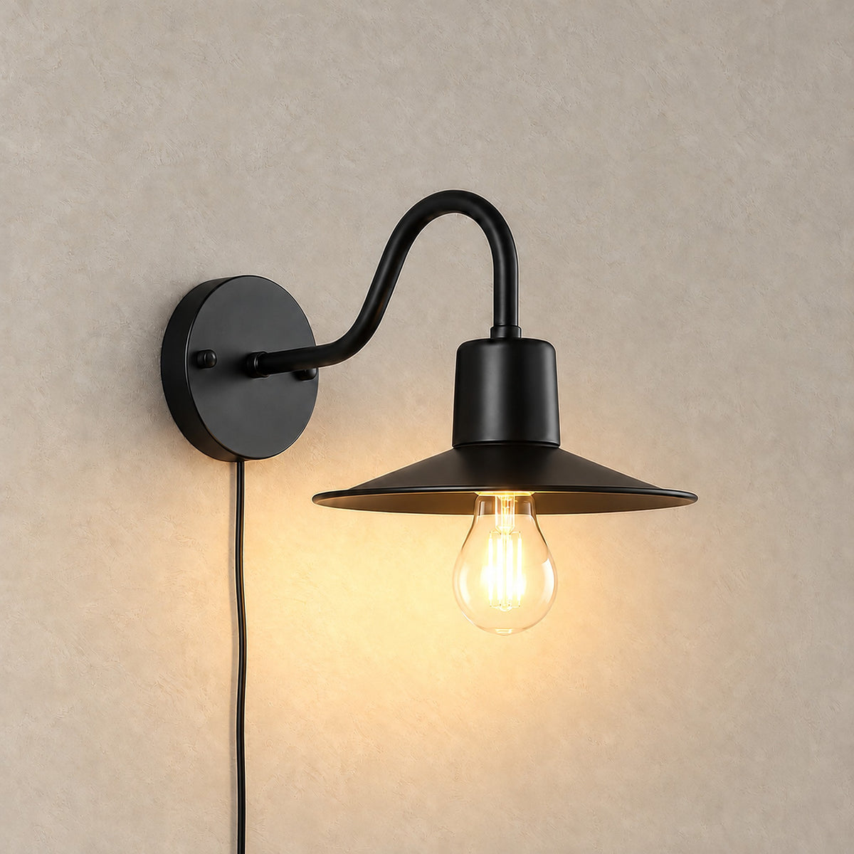 Tarelio black plug in wall lamp lit, its exposed vintage style bulb glowing under the shade