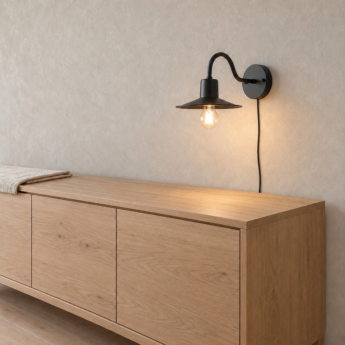 Tarelio black plug in wall light lit above a sideboard in a dining room by day