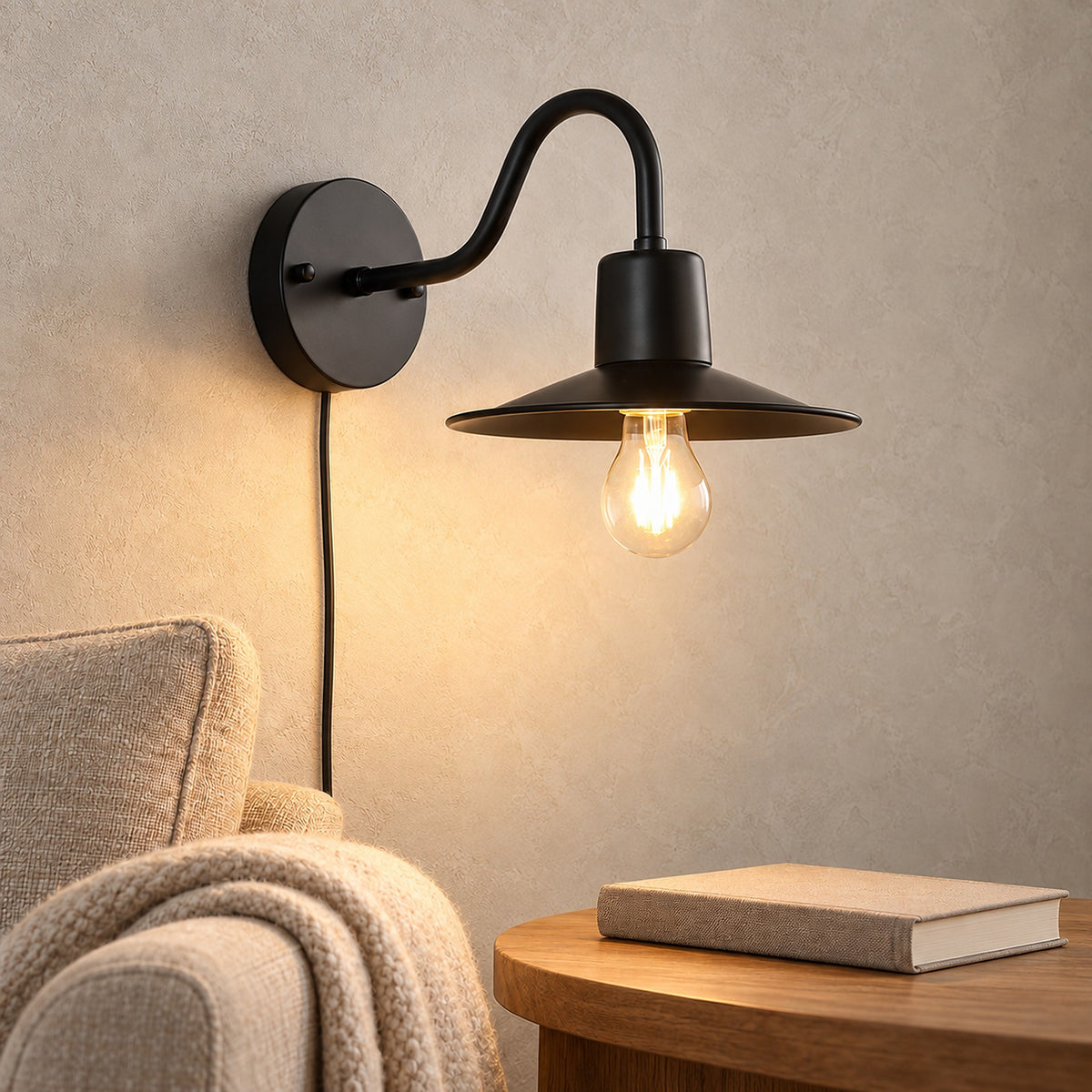 Tarelio black wall light glowing beside an oatmeal armchair in a reading corner by day