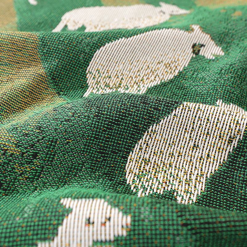 Close up of Timarno woven sheep throw blanket draped in folds, showing green fabric with white sheep motifs.