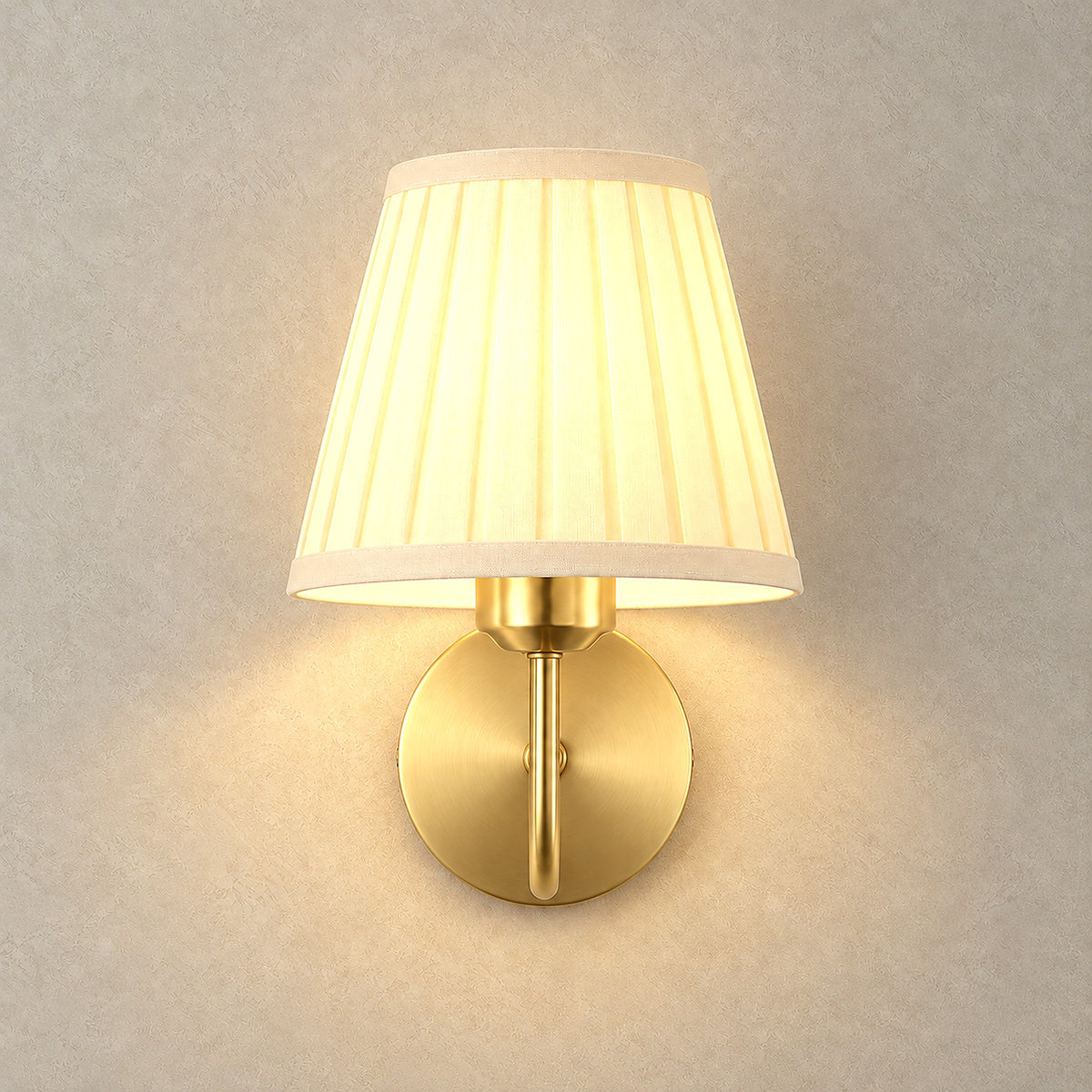 Tomirel gold wall sconce switched on, warm light glowing through every pleat of the fabric shade
