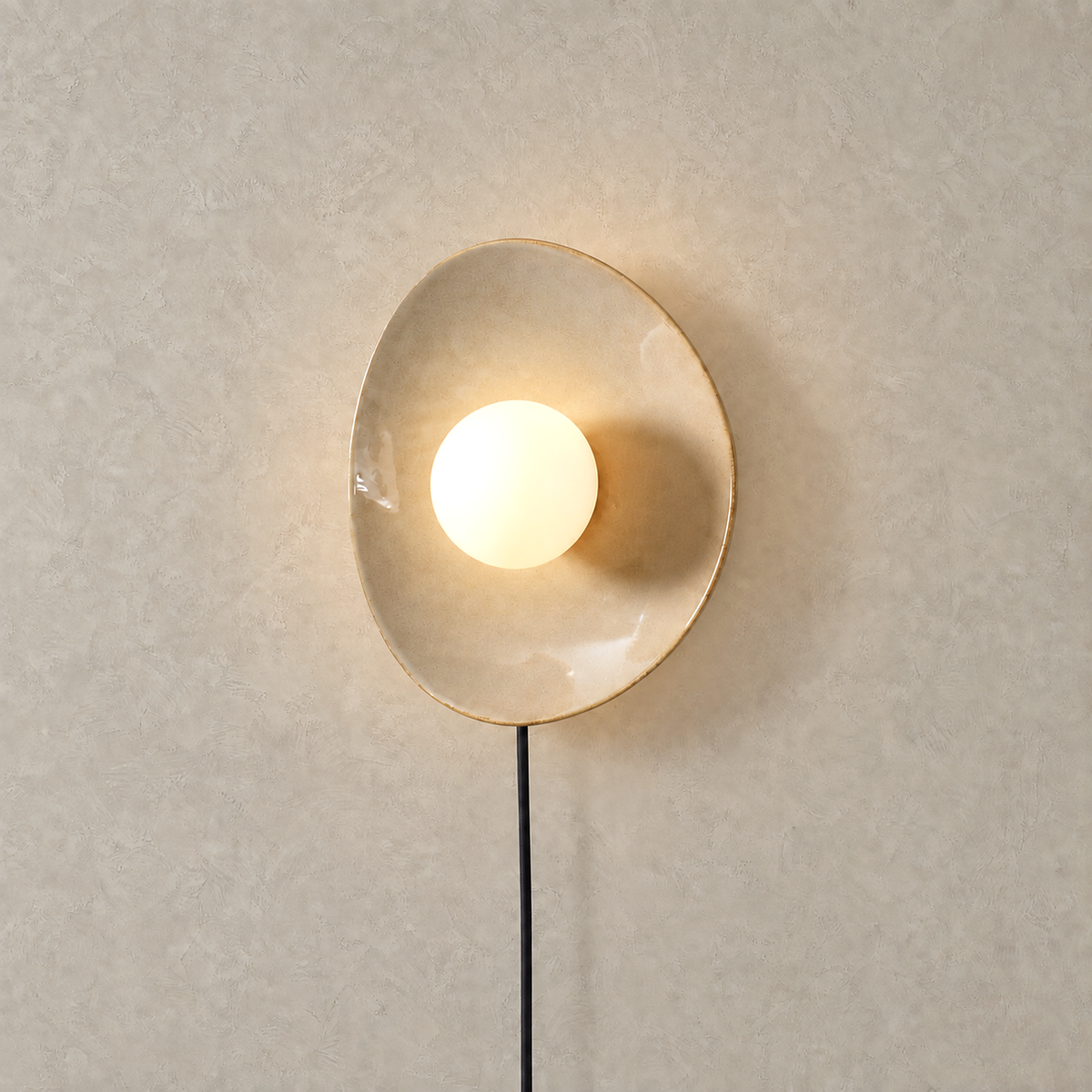 Venalti taupe LED wall sconce lit with a warm glow reflected back onto the wall