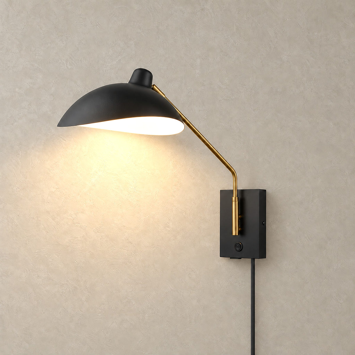 Vimolen black adjustable wall light with brass colored arm glowing against greige plaster